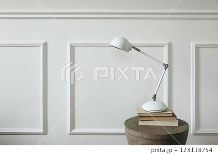 White modern table lamp standing on old books. Boho wooden curved coffee side table. Wall with elegant classic stucco decor. Empty copy space. Elegant Scandinavian living room interior, home. White modern table lamp standing on old books. Boho wooden curved coffee side table. Wall with elegant classic stucco decor. Empty copy space. Elegant Scandinavian living room interior, home. 123118754