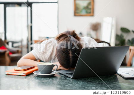 Tired woman with head on desk, surrounded by laptop, coffee, and notebook in a bright home office environment. Tired woman with head on desk, surrounded by laptop, coffee, and notebook in a bright home office environment. 123119600