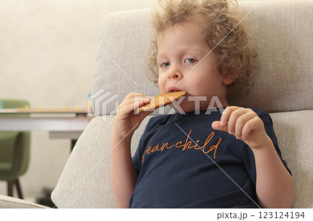 Little boy 3 years old in chair watching cartoon in room and eating biscuits. Children and lifestyle. Emotional Intelligence.  123124194
