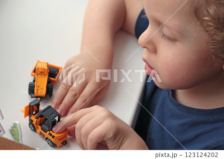 Little curly-haired blond boy playing with car on white table. Development games for children. Little curly-haired blond boy playing with car on white table. Development games for children. 123124202