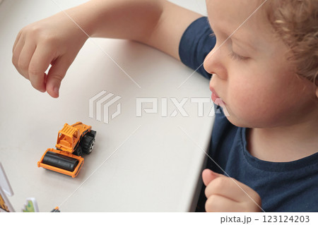 Little curly-haired blond boy playing with car on white table. Development games for children. Little curly-haired blond boy playing with car on white table. Development games for children. 123124203