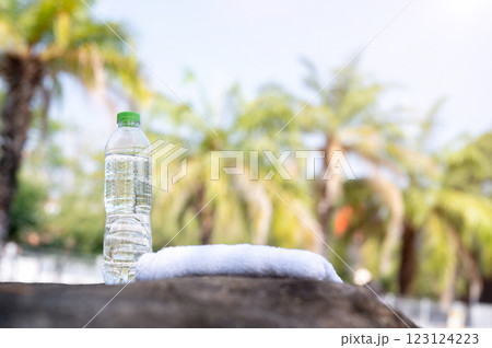 A water bottle place beside towel on the stone bench with blurry background of the coconut tree. A water bottle place beside towel on the stone bench with blurry background of the coconut tree. 123124223