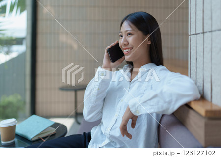 Happy young woman engaged in a phone conversation while relaxing in a bright modern cafe setting 123127102