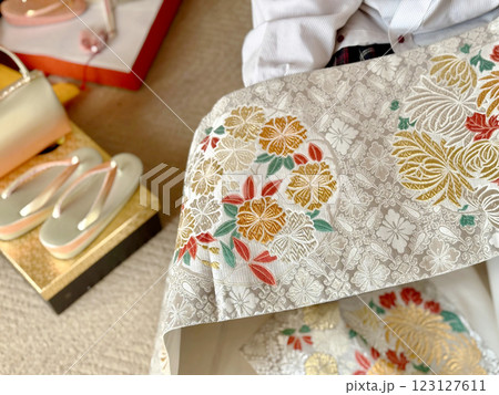 着物小物のそばで菊模様の銀色の帯を広げる女性 着物小物のそばで菊模様の銀色の帯を広げる女性 123127611