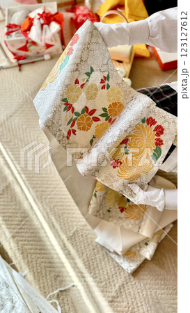 着物小物のそばで菊模様の銀色の帯を広げる女性_縦 着物小物のそばで菊模様の銀色の帯を広げる女性_縦 123127612