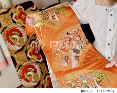 平安貴族柄の帯を広げる高齢女性の手元 123127613