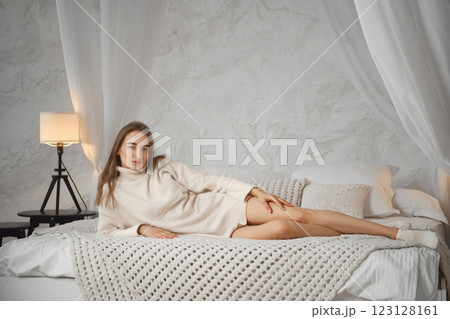 Cozy indoor setting with a woman relaxing on a bed in soft light 123128161