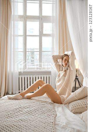 Charming woman relaxing in a cozy bedroom with soft natural light and delicate decor 123128167