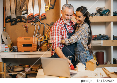 A couple of carpenters share loving embrace in their cozy woodshop, surrounded by tools and woodworking projects. As small business owners, enjoy working together, creating furniture and craft pieces 123128987