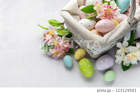 Pastel colored easter eggs overflowing from a white wicker basket decorated with spring flowers 123129581