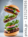 An impressive double-decker burger stacked with fresh lettuce, onions, cheese, and dripping sauce, with ingredients flying dramatically in the background, creating an exciting food explosion. 123129856
