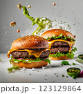 An impressive double-decker burger stacked with fresh lettuce, onions, cheese, and dripping sauce, with ingredients flying dramatically in the background, creating an exciting food explosion. 123129864