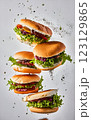 An impressive double-decker burger stacked with fresh lettuce, onions, cheese, and dripping sauce, with ingredients flying dramatically in the background, creating an exciting food explosion. 123129865
