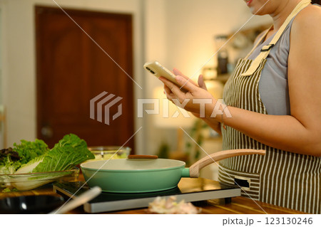 Middle aged woman checking a recipe on her mobile phone while cooking in the kitchen 123130246