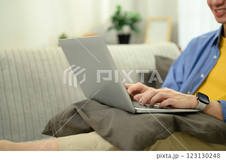 Smiling young Asian man working or browsing on a laptop in a cozy living room 123130248
