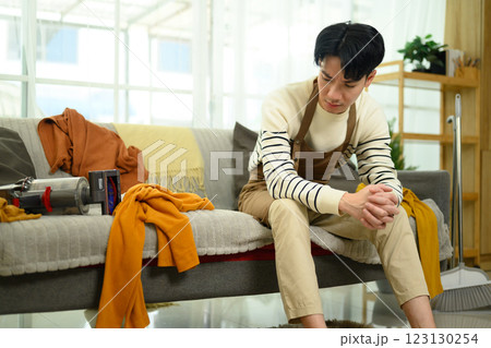 Exhausted man resting on the couch after cleaning with scattered clothes 123130254