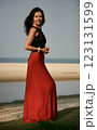 Portrait of a beautiful woman 51 years old posing in a red silk skirt and Indian earrings on the ocean shore Goa India 123131599