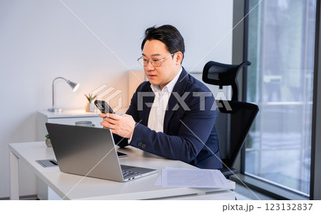 Professional Asian Businessman Reviewing Smartphone at Modern Office Desk Professional Asian Businessman Reviewing Smartphone at Modern Office Desk 123132837