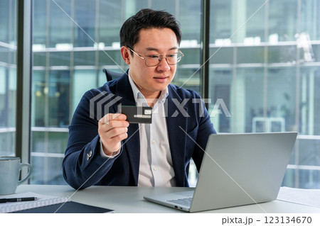 Confident Asian Businessman Shopping Online in Modern Office with Laptop 123134670