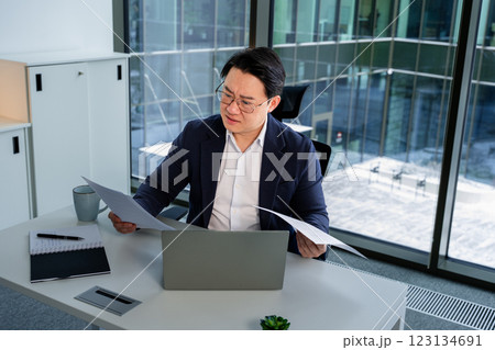 Professional Asian Businessman Analyzing Documents in Modern Office Setting 123134691