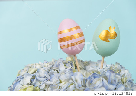 Two Easter painted eggs in a bouquet of flowers on a blue background, copy space for text Two Easter painted eggs in a bouquet of flowers on a blue background, copy space for text 123134818