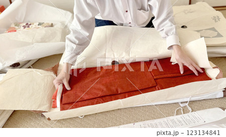 えんじ色の道行をたとう紙の上でたたむ女性の手元 えんじ色の道行をたとう紙の上でたたむ女性の手元 123134841