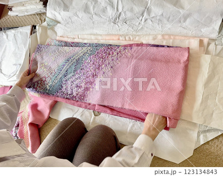 ピンク色の振り袖をたとう紙の上でたたむ女性の手元 123134843
