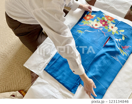 青色の中振り袖をたとう紙の上で広げる女性の手元 123134846