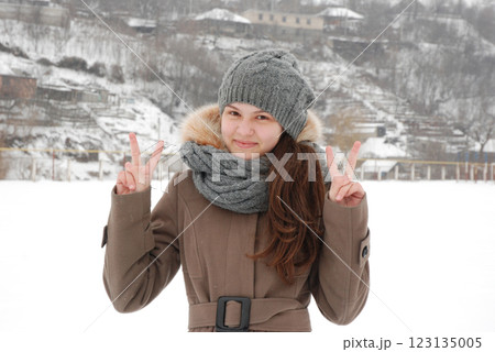 Winter portrait of a smiling girl in a cozy outfit with snowy background 123135005