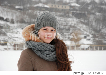 Winter portrait of a smiling woman in snowy landscape wearing grey knit hat and scarf 123135007