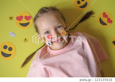 Sets of various paper emoji icons are pasted on the cheeks of the surprised girl. Social media of modern youth. Sets of various paper emoji icons are pasted on the cheeks of the surprised girl. Social media of modern youth. 123135018