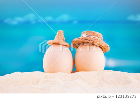 Happy easter. White eggs with hats on sandy beach of sea or ocean. Holiday postcard in hot country. Travel, spring, summer, vacations. Copy space 123135275