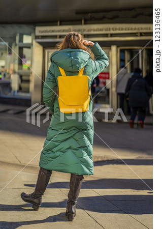 Woman in a green winter coat with a yellow backpack walking towards a subway entrance. Concept of urban transportation, daily commute, city life, modern woman Woman in a green winter coat with a yellow backpack walking towards a subway entrance. Concept of urban transportation, daily commute, city life, modern woman 123136465