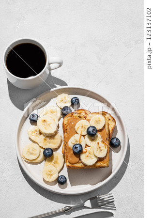 Peanut butter toast on a plate with banana and blueberry on a light background Peanut butter toast on a plate with banana and blueberry on a light background 123137102