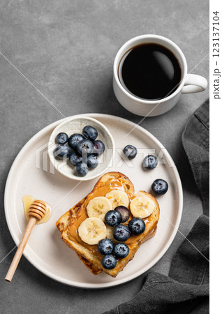 Peanut butter toast with banana, blueberry and honey on a plate on a dark  background 123137104