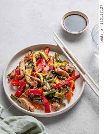 Stir-fry with vegetables and meat on wooden board on white background with chopsticks 123137127