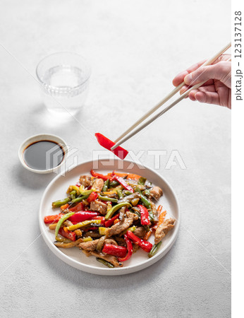 Hands holding chopsticks with stir-fry vegetables and meat on white background Hands holding chopsticks with stir-fry vegetables and meat on white background 123137128