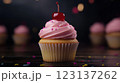 Vanilla cupcake with deep pink frosting and glossy red cherry, moody lighting enhancing golden cake crumb, placed on dark textured wooden backdrop with scattered colorful sprinkles, blurred background 123137262
