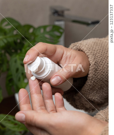 Woman in brown bathrobe pumping cream on finger and holding a cosmetic bottle in bathroom 123137337