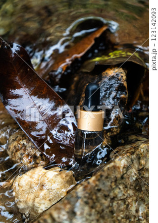 A hydration serum bottle sits on stone, surrounded by leaves and flowing water. A hydration serum bottle sits on stone, surrounded by leaves and flowing water. 123142093