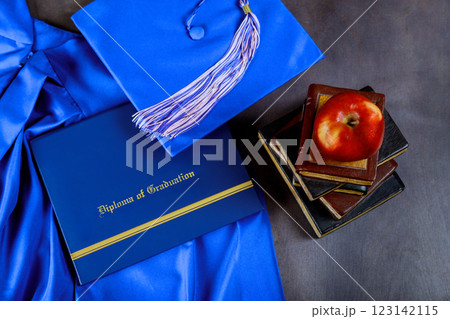 Graduation attire, diploma are arranged with books, fresh apple, symbolizing achievement, learning. 123142115