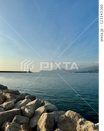 Vertical view of Bar, Montenegro, in warm sunset light with clear blue sky snd seascape, a distant horizon line, a lighthouse, and mountains in the background 123143160