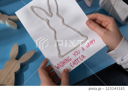 Person holding handmade greeting card with message WISHING YOU HAPPY EASTER written in beautiful handwriting. Gesture shows excitement and joy for the upcoming event. Springtime holiday gift present Person holding handmade greeting card with message WISHING YOU HAPPY EASTER written in beautiful handwriting. Gesture shows excitement and joy for the upcoming event. Springtime holiday gift present 123143181