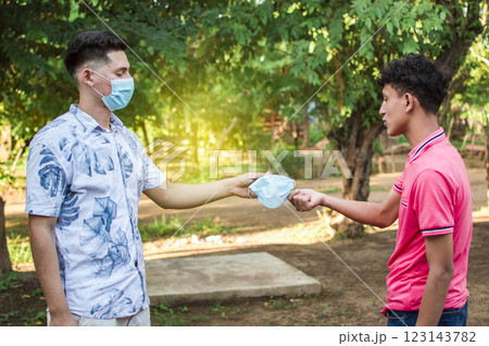 Two young people giving each other a mask, image of a young man giving a mask to another person, concept of a person offering a mask 123143782