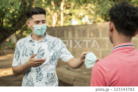 young man sharing mask to another young man, young man giving a mask to another young man, concept of giving a mask, 123143783
