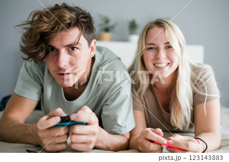 Young couple in love playing video games while lying on the bed in the bedroom, having fun and enjoying each other on their weekends. Technologies and gaming concept 123143883