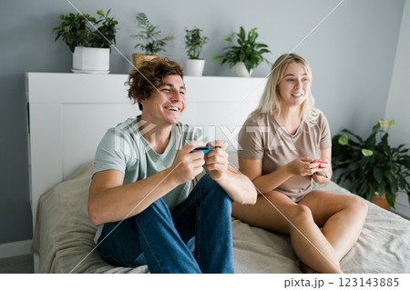 Young couple in love playing video games while lying on the bed in the bedroom, having fun and enjoying each other on their weekends. Technologies and gaming concept Young couple in love playing video games while lying on the bed in the bedroom, having fun and enjoying each other on their weekends. Technologies and gaming concept 123143885