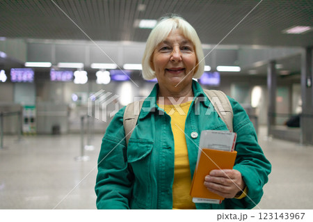 Traveler tourist happy smiling joyful fun mature elderly senior lady woman 55 years old with hand luggage, backpack holds passport and waits for flight travel at international airport terminal. Traveler tourist happy smiling joyful fun mature elderly senior lady woman 55 years old with hand luggage, backpack holds passport and waits for flight travel at international airport terminal. 123143967