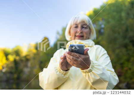 Positive elderly tourist woman searching location in map online on smartphone. Lifestyle, travel, tourism, active life.  123144032