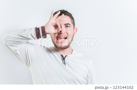 Funny young man making OK gesture looking through fingers isolated. Happy guy making ok gesture looking through fingers Funny young man making OK gesture looking through fingers isolated. Happy guy making ok gesture looking through fingers 123144102